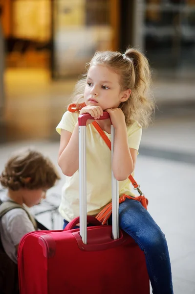 Charmiga girlie 7-8 år sitter bredvid sitt bagage på stationen. Stockfoto