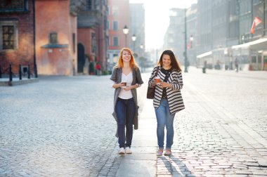 İki çekici kız turist elinde bir kahve ile eski şehrin sokaklarında yürümek.