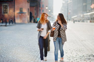 İki çekici kız turist elinde bir kahve ile eski şehrin sokaklarında yürümek.