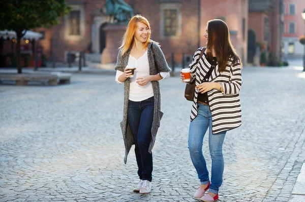 İki çekici kız turist elinde bir kahve ile eski şehrin sokaklarında yürümek. — Stok fotoğraf