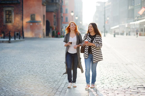 Twee aantrekkelijke meisjes toeristen lopen de straten van de oude stad met een kopje koffie in de hand. — Stockfoto