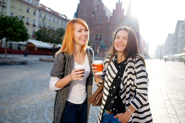 Två unga kvinnor är glada att dricka kaffe i centrum av den vackra europeiska staden. — Stockfoto