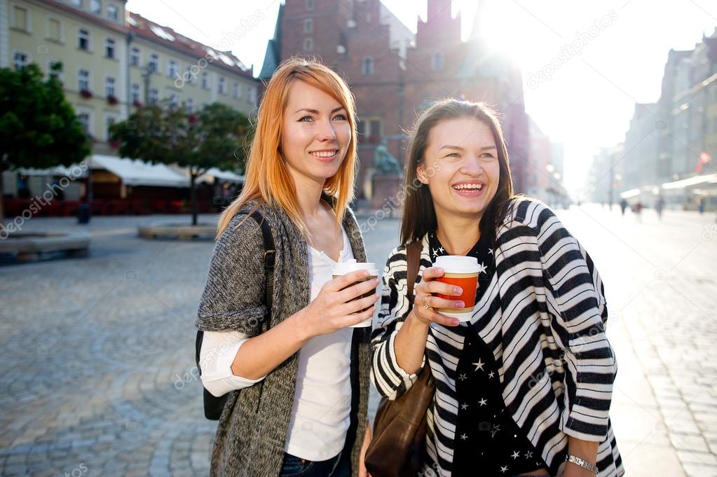 Two attractive girls tourists walk the streets of the old town with a coffee in hand.