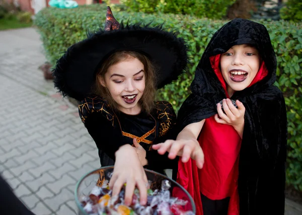Αγόρι και κορίτσι με μαύρα κοστούμια για τις Απόκριες δίνουν τα χέρια σε ένα βάζο με γλυκά. — Φωτογραφία Αρχείου