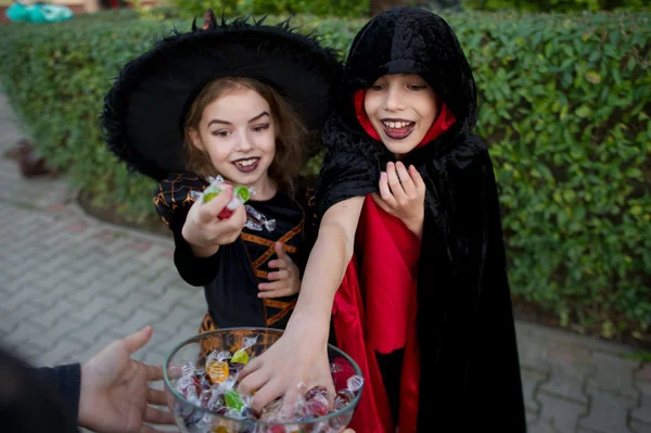 Αγόρι και κορίτσι με μαύρα κοστούμια για Απόκριες πάρει καραμέλες από ένα βάζο. — Φωτογραφία Αρχείου