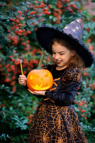 Nettes Mädchen von 8-9 Jahren im Anzug zu Halloween mit Kürbis und Zauberstab in der Hand. — Stockfoto