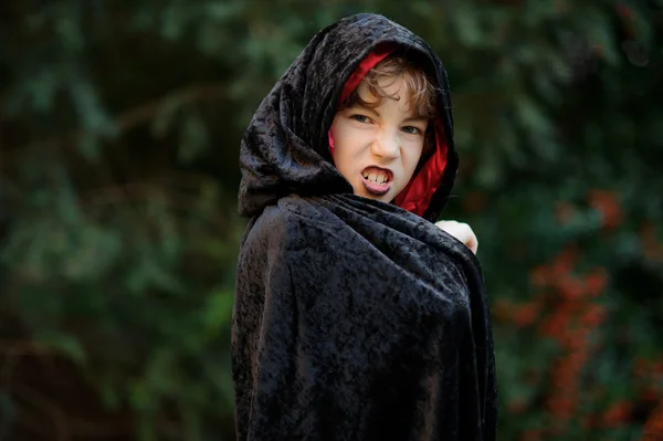 Garçon de plus jeune âge scolaire dans un manteau noir-rouge dépeint le sorcier maléfique . — Photo