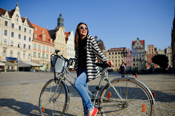 Cute young brunette in sunglasses with bicycle on a paved pavement.