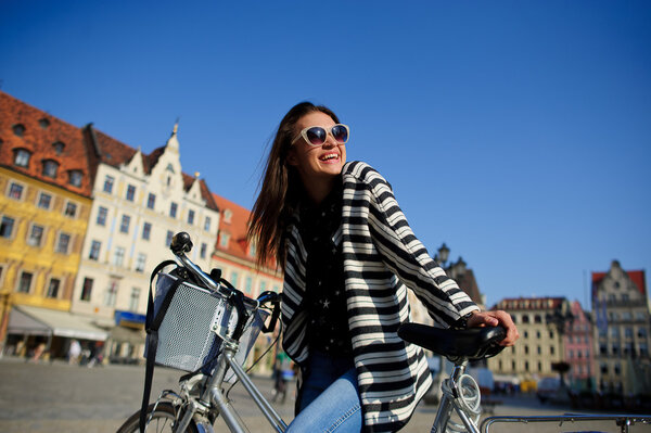 The young brunette in sunglasses with bicycle in the center of the ancient city