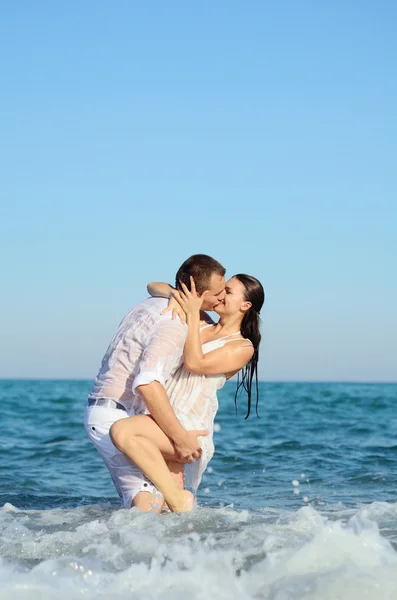 Jong koppel knuffelen op het strand in de golven — Stockfoto