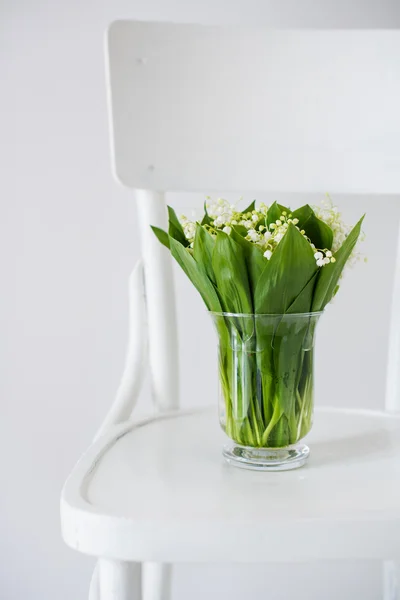 Liljekonvaljer i vas på en rustik stol — Stockfoto