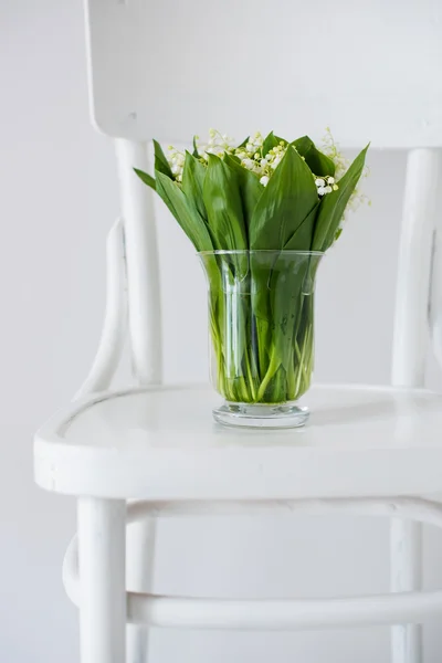 Lelies van de vallei in vaas op een rustieke stoel — Stockfoto