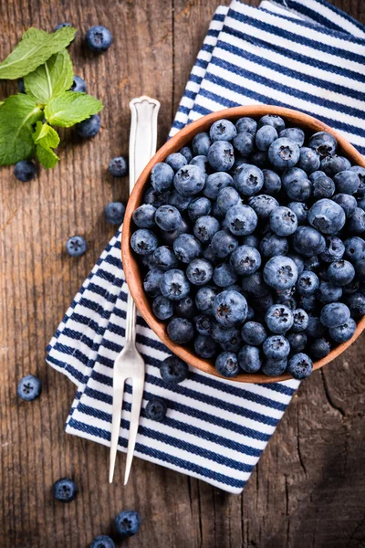 Volle Schüssel mit frischen reifen Blaubeeren auf altem Holzbrett — Stockfoto