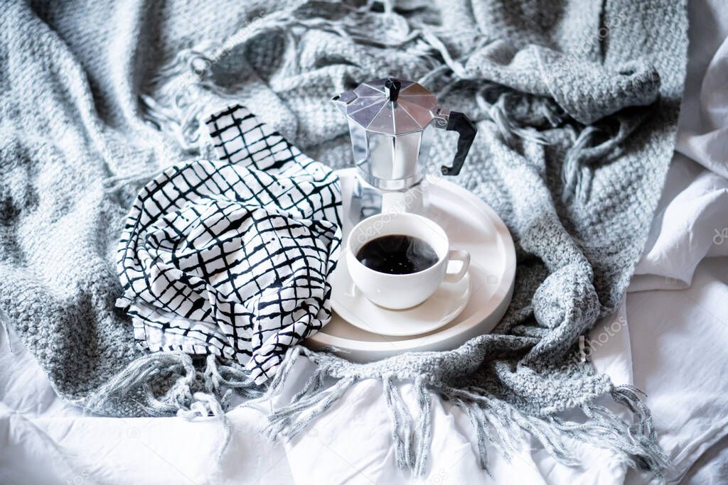 Cup of coffee on tray in cozy winter bad with wool blanket