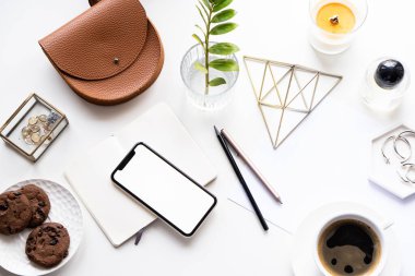 Akıllı telefon modeli, kahve fincanı ve not defteri olan beyaz ofis masası.