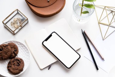 Akıllı telefon modeli, kahve fincanı ve not defteri olan beyaz ofis masası.