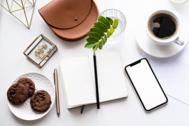 Akıllı telefon modeli, kahve fincanı ve not defteri olan beyaz ofis masası.