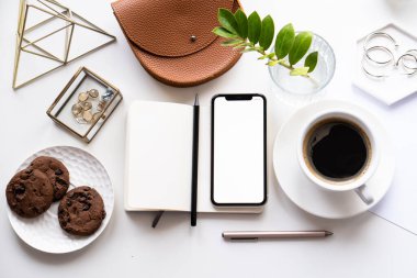 Akıllı telefon modeli, kahve fincanı ve not defteri olan beyaz ofis masası.