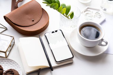 Akıllı telefon modeli, kahve fincanı ve not defteri olan beyaz ofis masası.