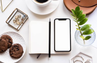 Akıllı telefon modeli, kahve fincanı ve not defteri olan beyaz ofis masası.