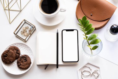 Akıllı telefon modeli, kahve fincanı ve not defteri olan beyaz ofis masası.