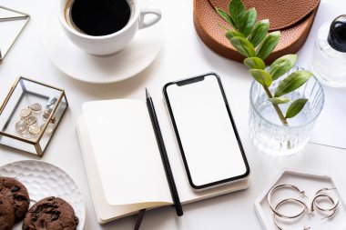 Akıllı telefon modeli, kahve fincanı ve not defteri olan beyaz ofis masası.