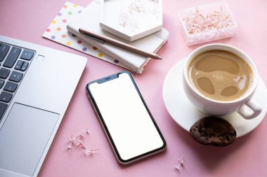 Bayan Freelancers evde pastel pembe işyeri, bir fincan kahve ve akıllı telefon modeli.