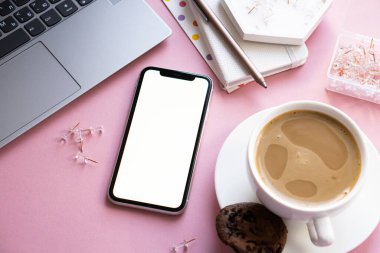 Bayan Freelancers evde pastel pembe işyeri, bir fincan kahve ve akıllı telefon modeli.