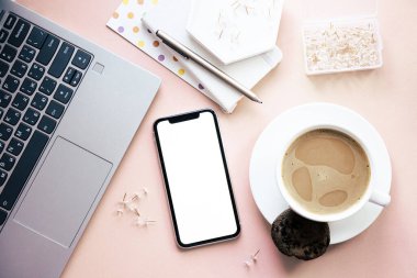 Bayan Freelancers evde pastel pembe işyeri, bir fincan kahve ve akıllı telefon modeli.