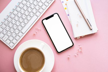 Bayan Freelancers evde pastel pembe işyeri, bir fincan kahve ve akıllı telefon modeli.