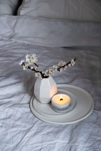 Kvetoucí meruňkové větve stromů a hořící svíčka na kulatém podnosu v ložnici interiér, bílá jarní domácí dekorace — Stock fotografie