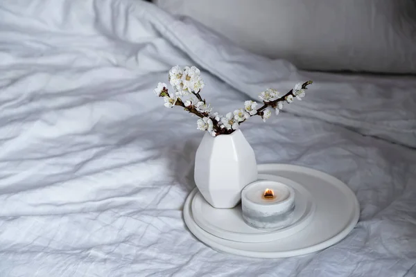 Florecientes ramas de albaricoque y vela ardiente en bandeja redonda en el interior del dormitorio, decoración casera de primavera blanca —  Fotos de Stock
