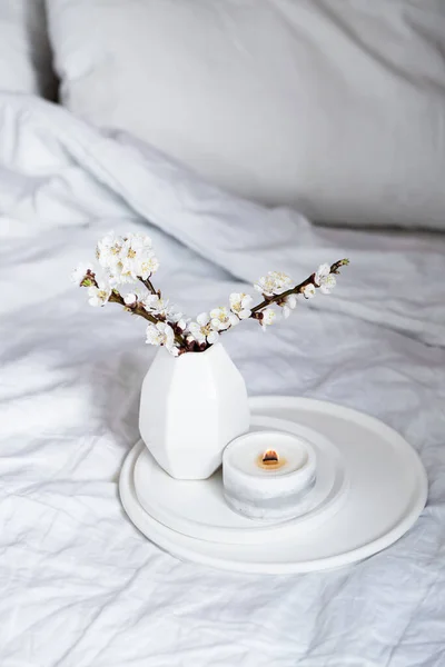 Blooming apricot tree branches and burning candle on round tray in bedroom interior, white spring home decoration — Stock Photo, Image