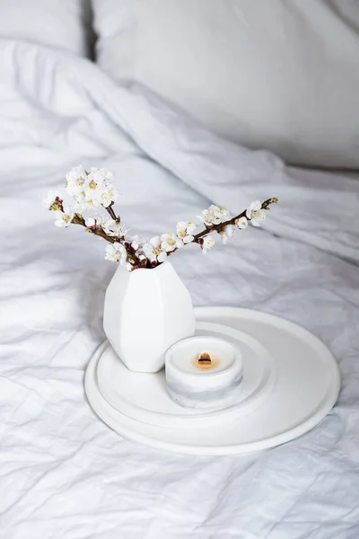 Florecientes ramas de albaricoque y vela ardiente en bandeja redonda en el interior del dormitorio, decoración casera de primavera blanca —  Fotos de Stock