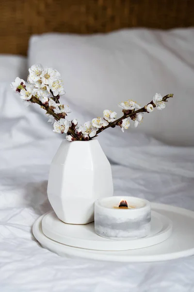 Florecientes ramas de albaricoque y vela ardiente en bandeja redonda en el interior del dormitorio, decoración casera de primavera blanca — Foto de Stock