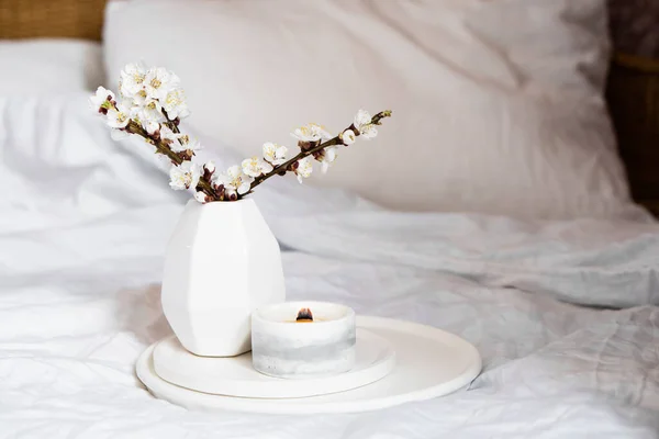 Blooming apricot tree branches and burning candle on round tray in bedroom interior, white spring home decoration — Stock Photo, Image