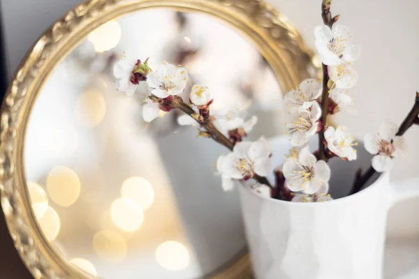 Blooming apricot tree branches in cup and burning candle in front of mirror — Stock Photo, Image