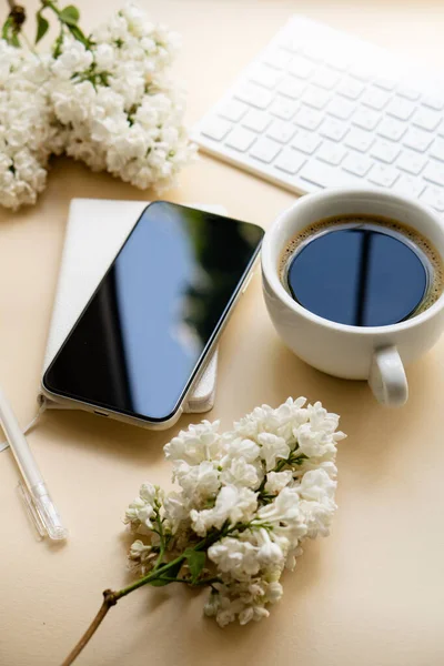 Neutral color tabletop with keyboard, white lilac flowers and black smartpohone — Stockfoto