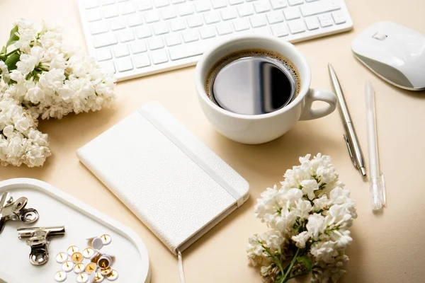 Bézs és fehér munkaterület kávéscsészével, jegyzettömbbel és lila virágokkal — Stock Fotó