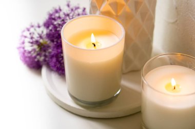 Beyaz tepside yanan mum ve menekşe çiçekleri.