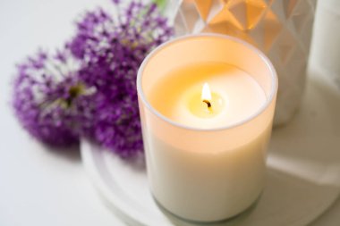 Beyaz tepside yanan mum ve menekşe çiçekleri.