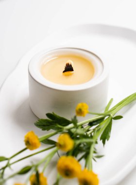 Beyaz yanan mum, ahşap fitil ve sarı çiçekler beyaz tepside