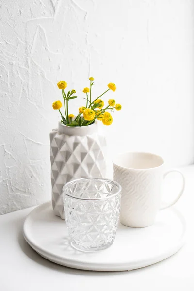 Décoration de maison blanche avec fleurs jaunes, vase en céramique et verre sur plateau — Photo