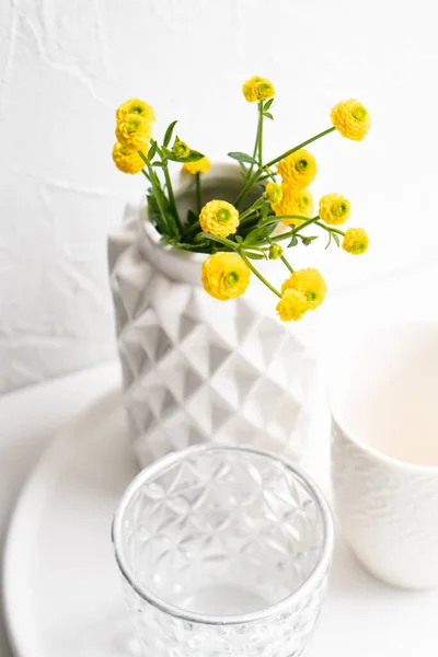 Sarı çiçekli beyaz ev dekorasyonu, seramik vazo ve tepside cam. — Stok fotoğraf