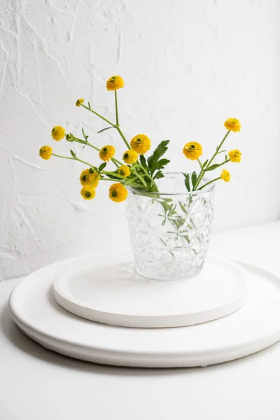 Białe dekoracje wnętrz z żółtymi kwiatami, ceramicznym wazonem i szkłem na tacy — Zdjęcie stockowe