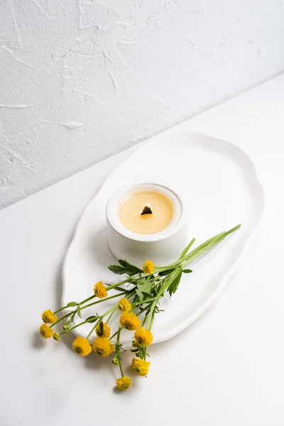 Vela blanca ardiente con mecha de madera y flores amarillas en bandeja blanca —  Fotos de Stock
