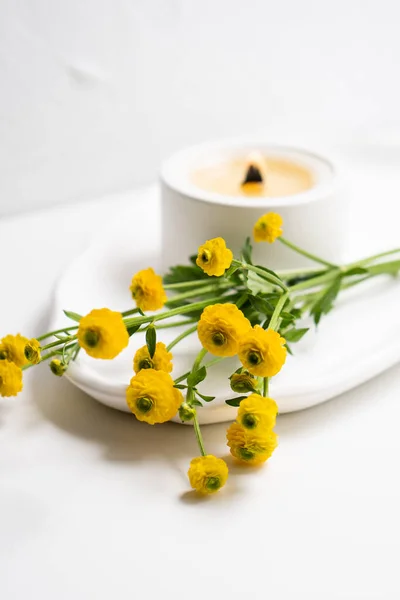 Biała świeca z drewnianym knotem i żółtymi kwiatami na białej tacy — Zdjęcie stockowe