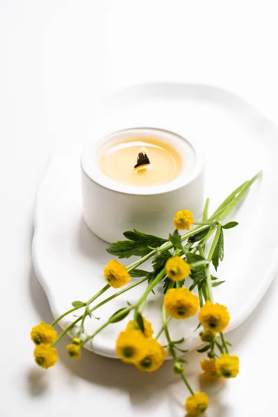 Λευκό λαμπάδα με ξύλινο φυτίλι και κίτρινα λουλούδια σε λευκό δίσκο — Φωτογραφία Αρχείου