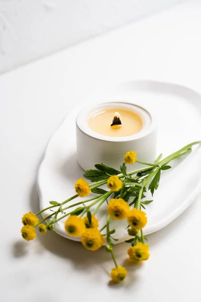Vela blanca ardiente con mecha de madera y flores amarillas en bandeja blanca —  Fotos de Stock