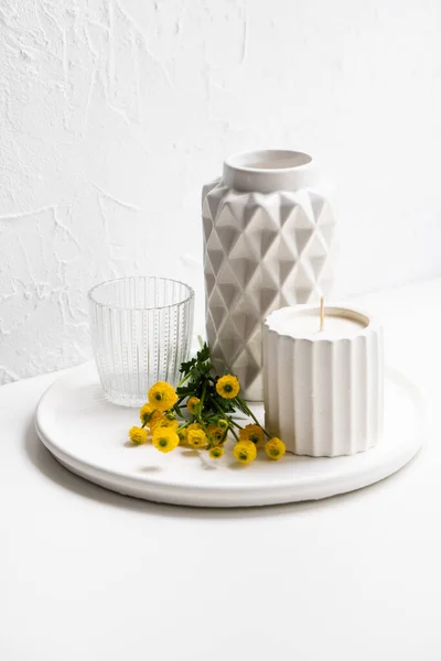 Διακόσμηση σε λευκό σπίτι με κίτρινα λουλούδια, κεραμικό βάζο, κερί και γυαλί στο δίσκο — Φωτογραφία Αρχείου